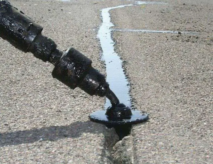 Hot crack sealant flowing from a Crafco wand into a pavement crack.