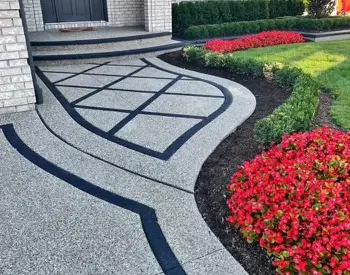 Exposed-aggregate concrete walkway with curving black accent lines and red flowers.
