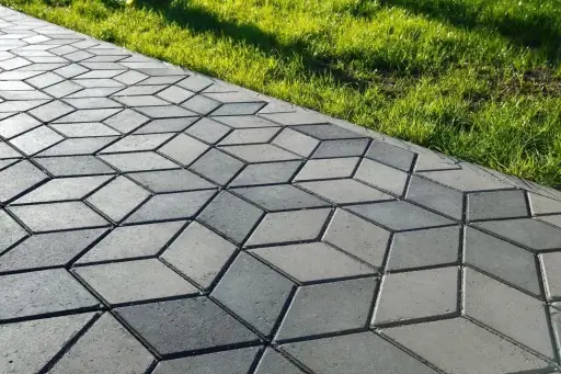 Diamond-pattern concrete pavers forming a walkway alongside a green lawn.