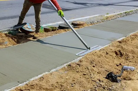 A CAP worker finishing wet concrete with a long-handled bull float.