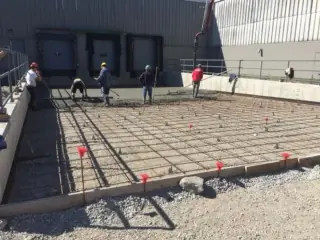 A fresh concrete pad being poured over a rebar grid by a crew of workers.
