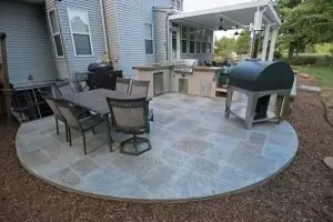 A stamped concrete patio in flagstone pattern with patio furniture and a built-in grill.